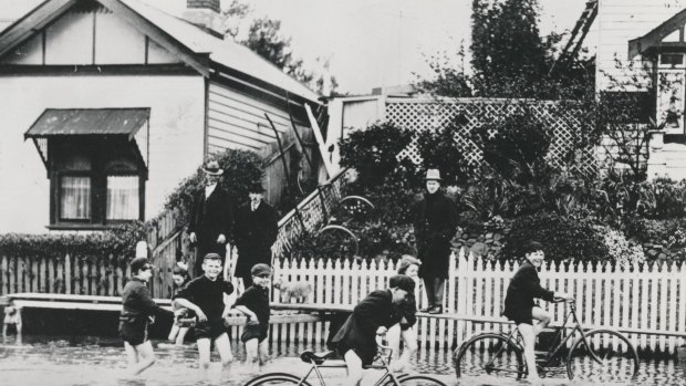 A group of children ride bicycles flood waters.