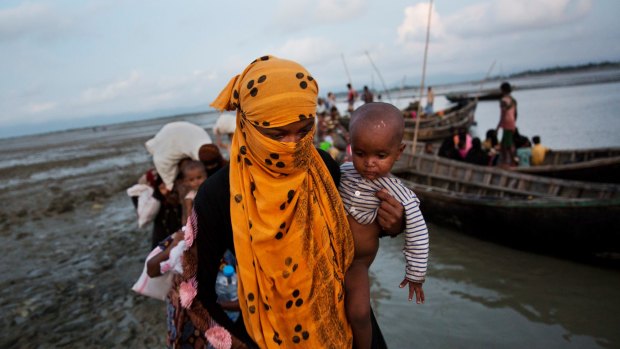 A Rohingya woman carries a child after crossing a stream on a small boat near Cox's Bazar's Dakhinpara area in Bangladesh. 