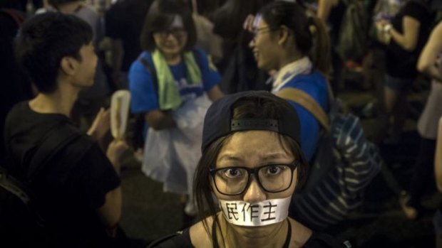 A protester covers her mouth with tape that says "democracy".
