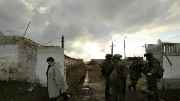 A woman walks past Russian forces near the entrance of the Ukrainian military base in Perevalnoye.