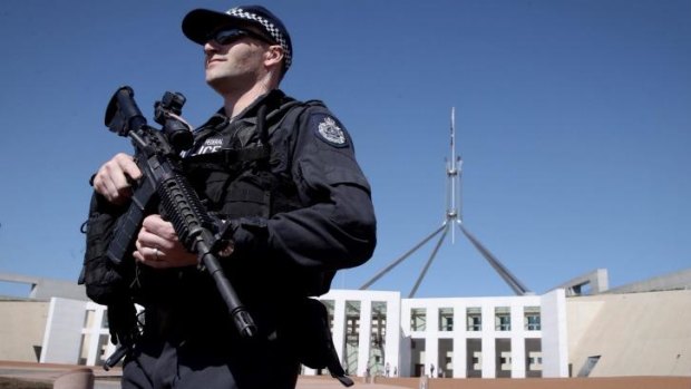 An AFP officer armed with a machine gun patrols outside the front of Parliament House.