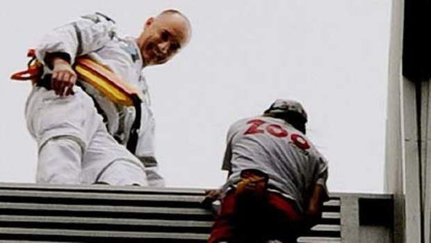 A police officer waits with a smile to take Alain Robert into custody at the end of his 57-storey climb.