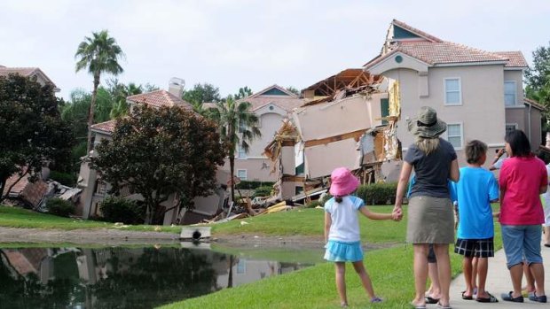 People look at a partially collapsed building over a sinkhole at Summer Bay Resort near Disney World in Clermont, Florida.