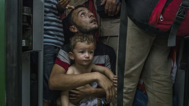 A migrant father holds his son as they wait for a train to leave at Keleti station in Budapest, Hungary, on Thursday.