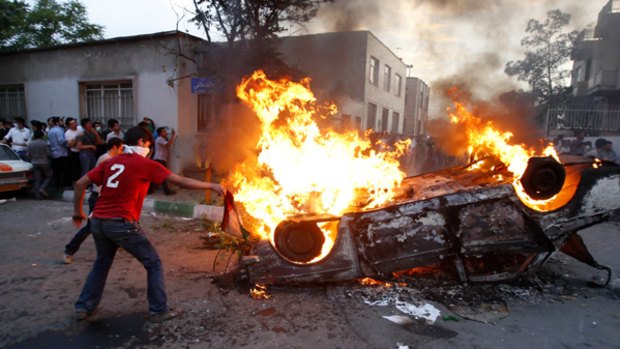 Demonstrators burn a car as protests turn violent.