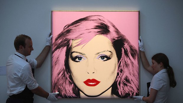 Two gallery technicians adjust a painting by Andy Warhol's 'Debbie Harry' in Sotheby's auction house in London.