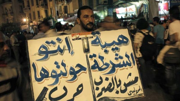 An Egyptian protester carries a placard in Arabic that translates as  "Violence does not gain the police respect, you started this war".