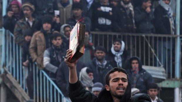An Afghan demonstrator holds a copy of a half-burnt Koran.