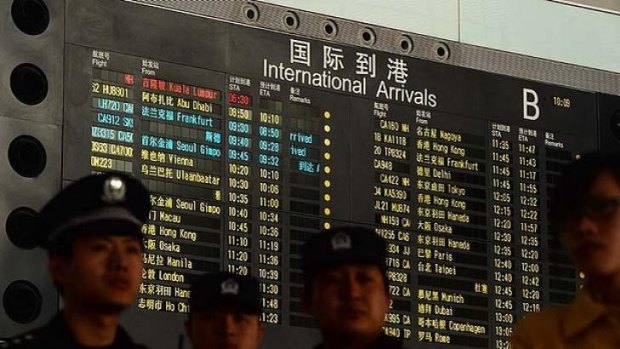 Chinese police in front of the arrival board showing Malaysia Airlines flight MH370 (top-red) at Beijing Airport.