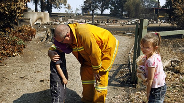 All that's left ... firefighter Steve Nash comforts his children Lachlan and Teagan as they stand in what remains of their Kinglake home. It burnt to the ground.