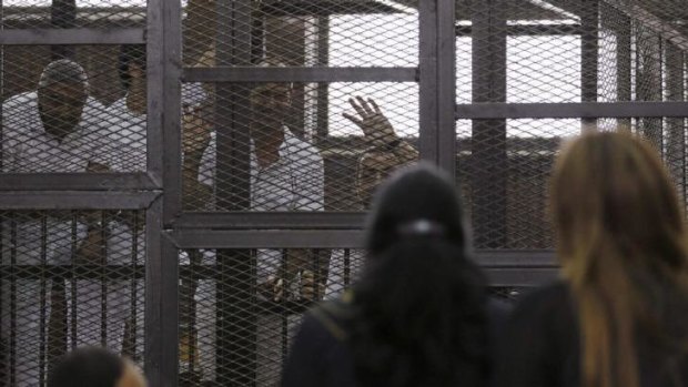 Al Jazeera journalists Mohammed Fahmy, Peter Greste and Baher Mohamed wave to family and friends during their trial in Cairo.  