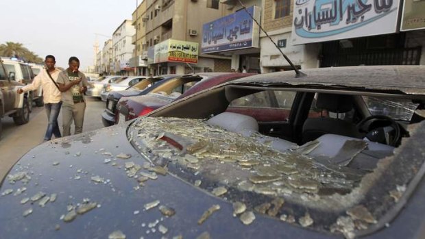 Men walk next to a car which was damaged during clashes between Saudi and foreign workers in Manfouha, southern Riyadh.