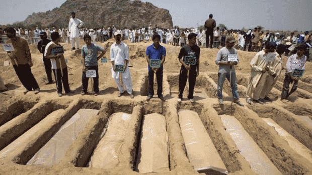 Members of the Ahmadi community stand over the graves of people slain in the attacks on two mosques.