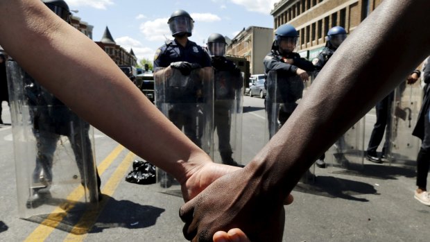 Members of the community hold hands in front of police officers in riot gear outside a recently looted and burned CVS store in Baltimore on Tuesday. 