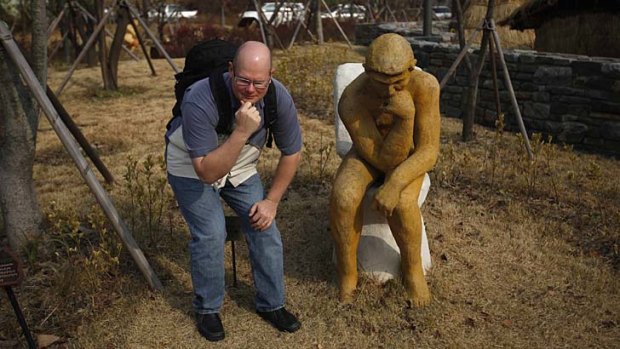A tourist poses next to an installation shaped like Auguste Rodin's sculpture "The Thinker" on a toilet, at the Toilet Culture Park in Suwon.