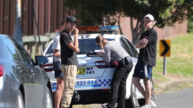 Police detectives talk to teenagers close to a house after a 15-year-old boy was shot in the head at a home in Glenfield. 
