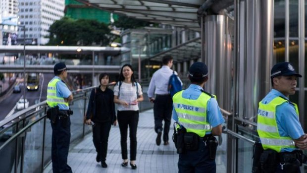 Police officers stand on a pedestrian bridge as commuters walk past in the Central district of Hong Kong, China.
