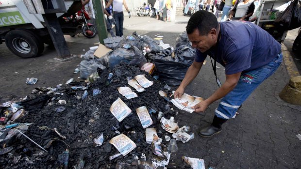 As a form of protest against the Venezuelan government, an unidentified man arranges singed flyers promoting an opposition congressional candidate on top of a trash pile in Caracas.