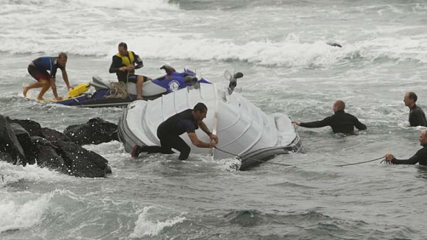 Police and rescuers try to salvage their upturned boat during a rescue.