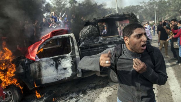 A university student  stands in front of a burning police vehicle during a demonstration in support of ousted president Mohammed Mursi.