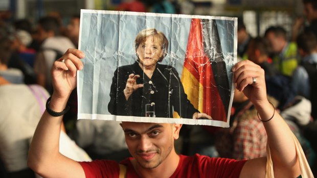 A migrant from Syria holds a picture of German Chancellor Angela Merkel as he and approximately 800 others arrive from Hungary at Munich Hauptbahnhof main railway station in Munich, Germany. 