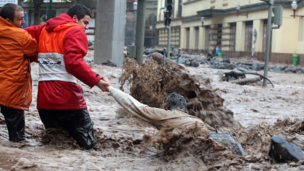 Rescuers help a man struggling to cross a flooded street in Funchal, the capital of Madeira.