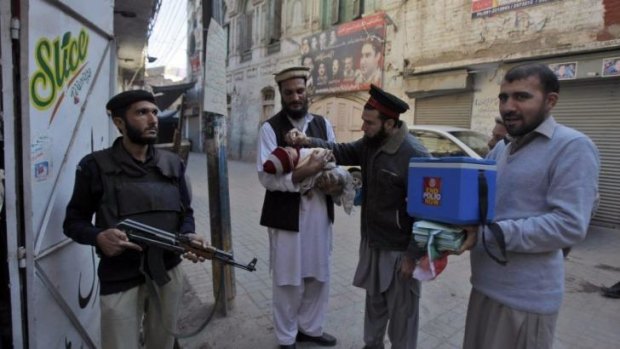 Wary of further attacks ... a Pakistani police man, left, stands guard as a health worker vaccinates a child against polio, in Peshawar, Pakistan. 