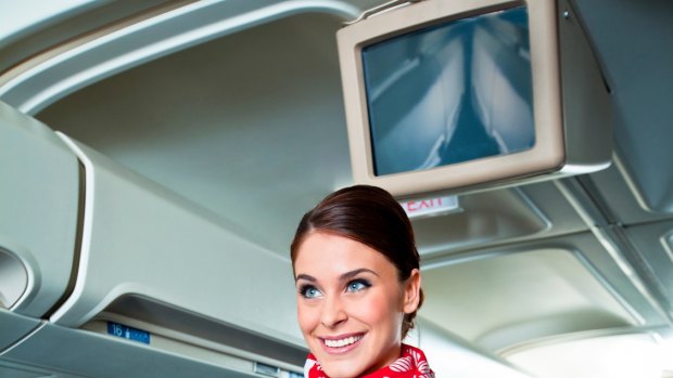 Beautiful flight attendant standing in an airplane and demonstrating a seat belts before taking off.