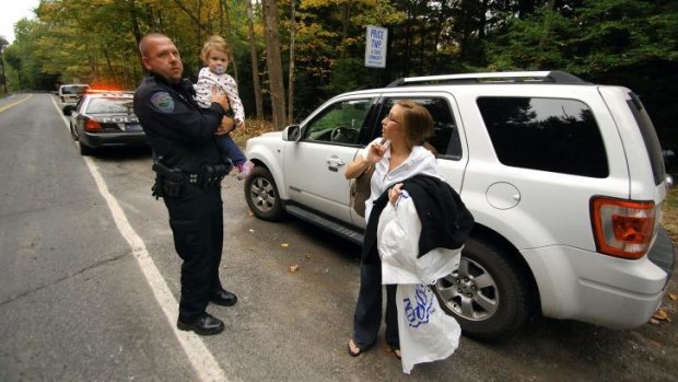 Barrett Township Police patrolman William Carey holds Riley Killinger, 2, as her mother Kerriann Sanders stands near their vehicle, after patrolman Carey picked them up from their house in Canadensis.