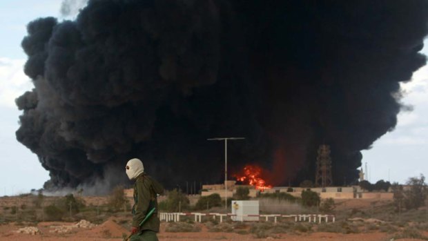 A rebel walks past a burning Al-Sedr Oil Terminal after it was hit by pro-Gaddafi forces.