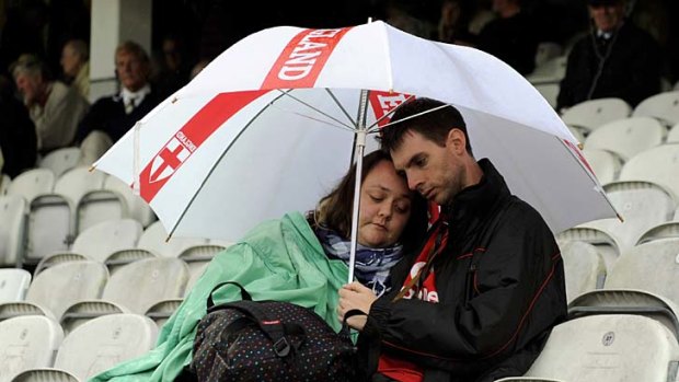 Two spectators shield under an umbrella as rain delayed the fourth cricket Test between England and India at the Oval.