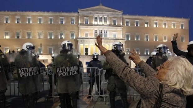 A woman gestures towards the Greek parliament as riot police stand guard during a protest in central Athens after a  man shot himself dead, leaving a suicide note that blamed the country's harsh austerity measures for his action.