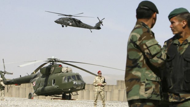 Afghan army soldiers watch as a US helicopter flies over a Polish helicopter at a military base in Ghazni province.