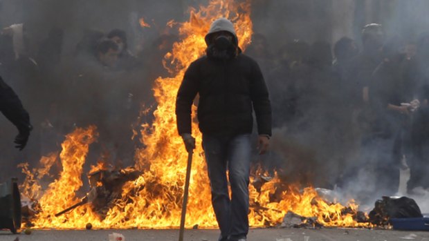An anarchist walks in front of burning trash during clashes in Athens on Sunday.