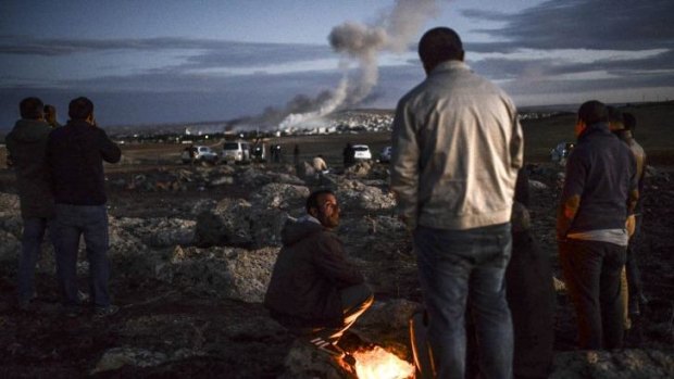 Kurdish people observe smoke rising from the Syrian town of Kobane, following an explosion as seen from the southeastern Turkish village of Mursitpinar.