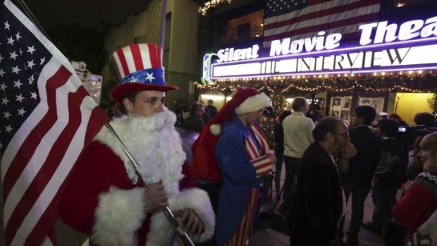 Matt Ornstein, dressed in a Santa Claus costume, holds an American flag as fans line up at the Silent Movie Theatre for a midnight screening of <i>The Interview</i>.