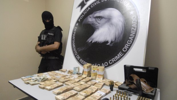 Brazil's police show arms, munitions and money allegedly confiscated from the home of legislator and television show host Wallace Souza, inset.
