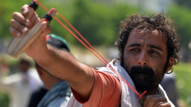 A protester fires a slingshot towards riot police during clashes in the Pakistani capital.