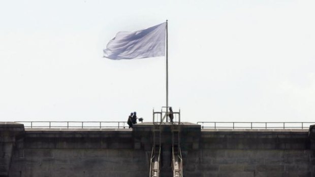 New York City Police officers stand at the base of a white flag flying atop the west tower of New York's Brooklyn Bridge.