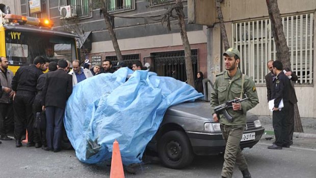A policeman walks past the car belonging to Iranian nuclear scientist Mostafa Ahmadi Roshan outside a university in northern Tehran.