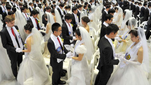 Newly-married couples hold hands to pray during a mass wedding organised by the Unification Church.