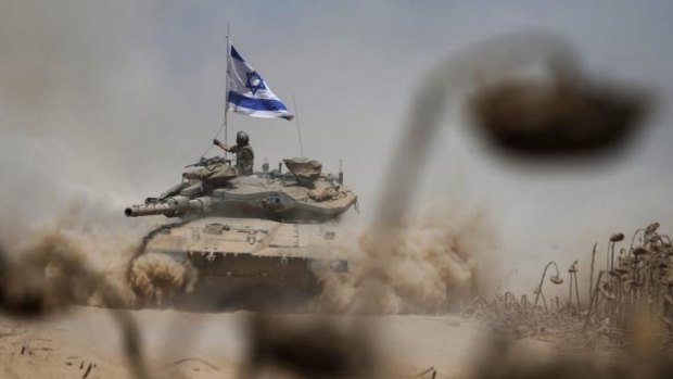 An Israeli soldier adjusts has flag as he rides atop a tank near the border after returning to Israel from Gaza.