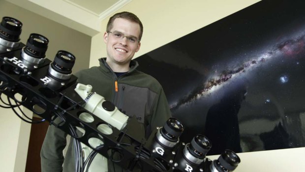 Nick Risinger poses with the rack of six synchronized astrophotography cameras he used to create the photograph on the wall behind him, which shows the entire night sky in a single composite image.