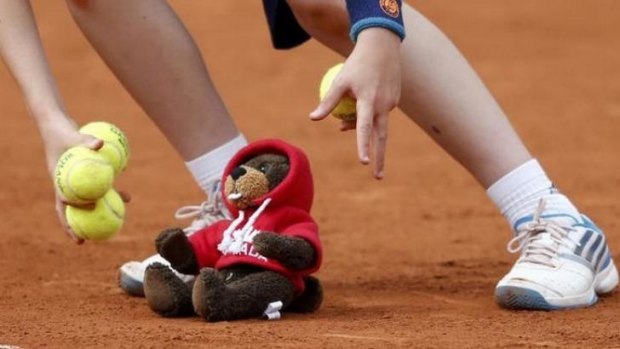 A ball boy picks up a teddy bear thrown on the court to support Eugenie Bouchard of Canada after she won her women's quarter-final match against Carla Suarez Navarro of Spain at the French Open.