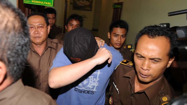 The Australian teenager facing drugs charges in Bali covers his face as he is escorted by guards at the prosecutor's office in Denpasar.