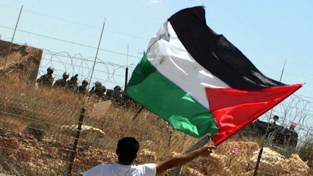A Palestinian demonstrator waves his national flag opposite Israeli soldiers during a protest.