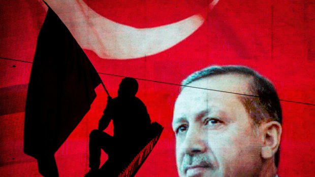 A supporter of Turkish President Recep Tayyip Erdogan waves a flag against an electronic billboard during a rally in Ankara, Turkey.
