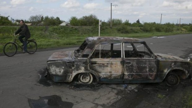 A cyclist rides by a burnt car at a crossroad that was the centre of fierce fighting between the Ukrainian army and pro-Russian rebels, near the town of Slaviansk.