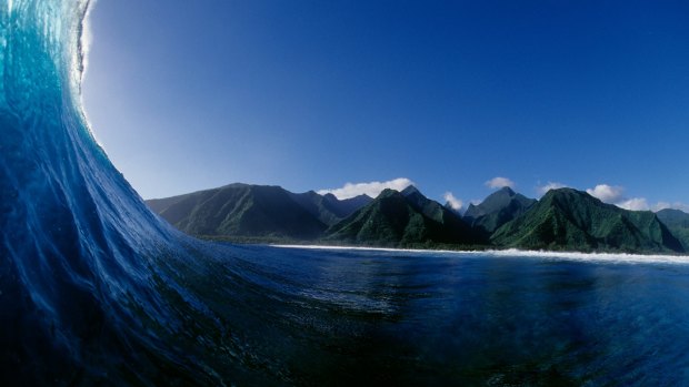 Surfer's view inside a breaking wave with lush green mountain backdrop in Tahiti.