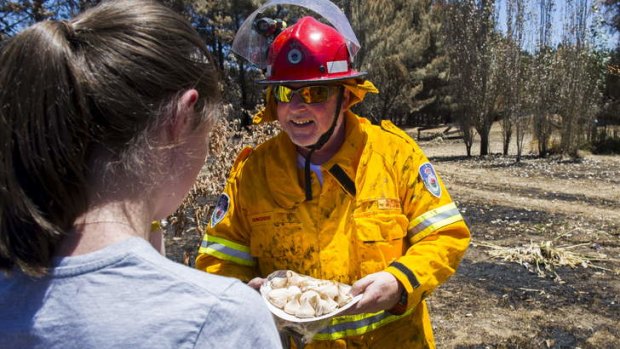 Bungendore RFS Captain, Sheldon Williams, accepts a plate of home-made meringues from Jacqui Coleman after extinguishing a burning stump at a property next to the Kings Highway near Bungendore.
